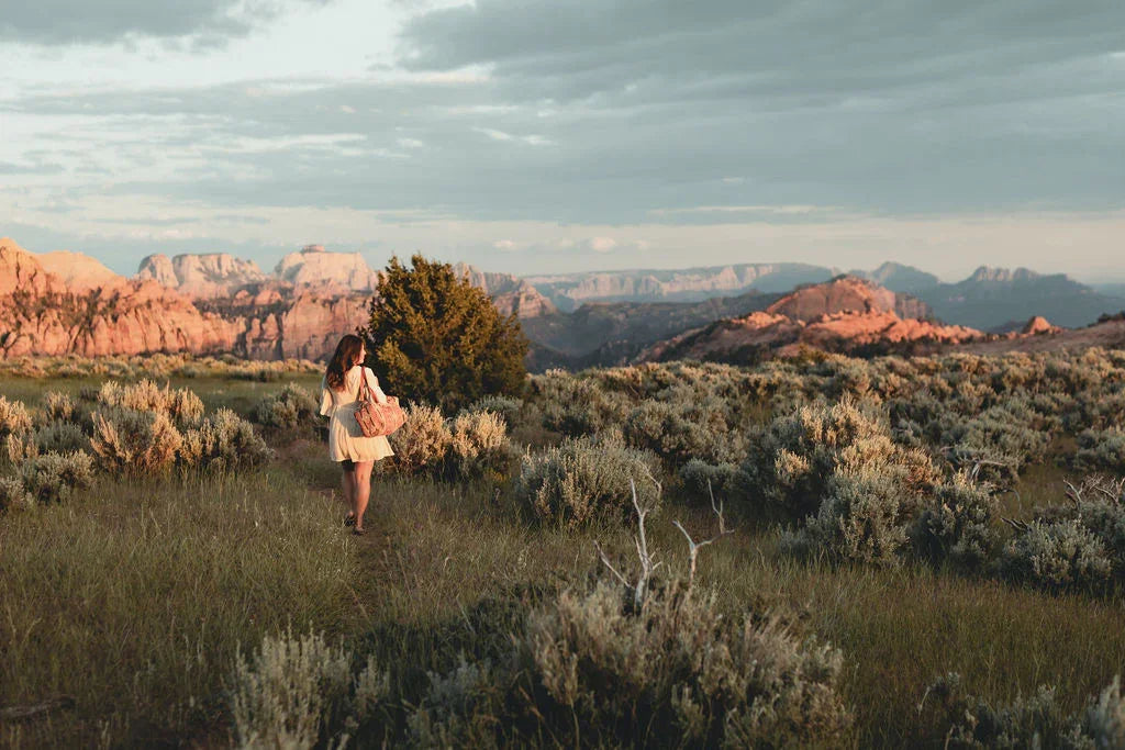 Woman walking in nature with a blanket, scenic mountains and sagebrush at sunset.