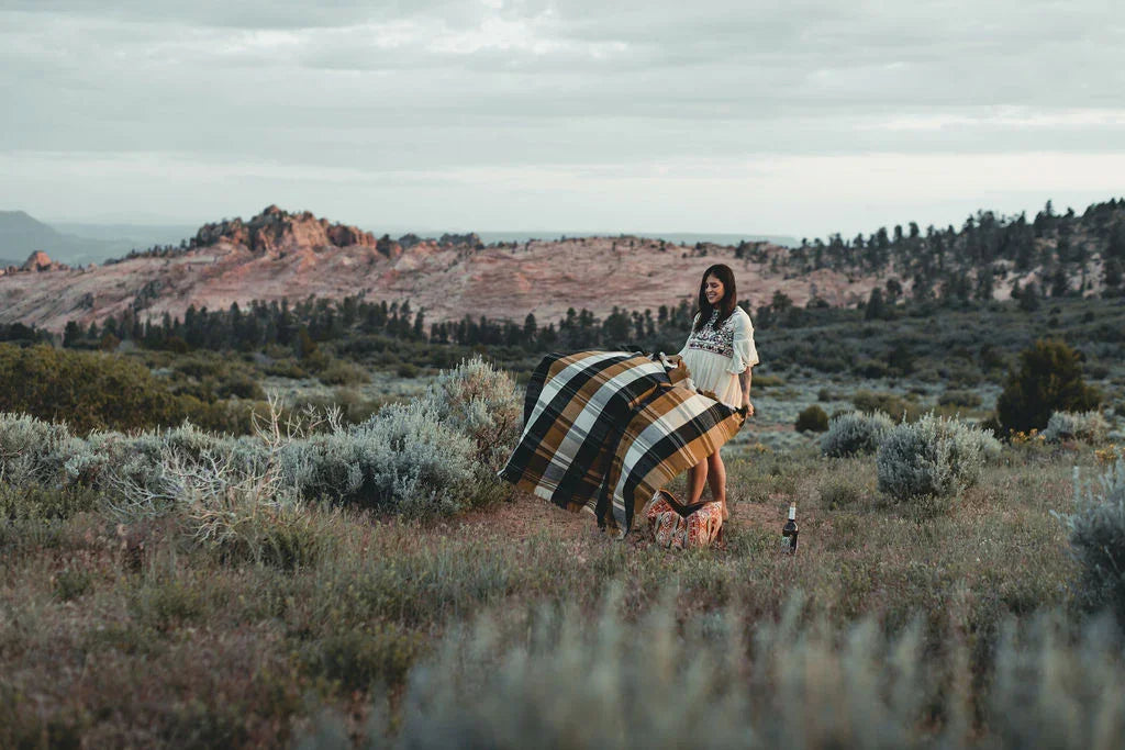 Woman holding cozy plaid blanket in scenic outdoor landscape with mountains and grass