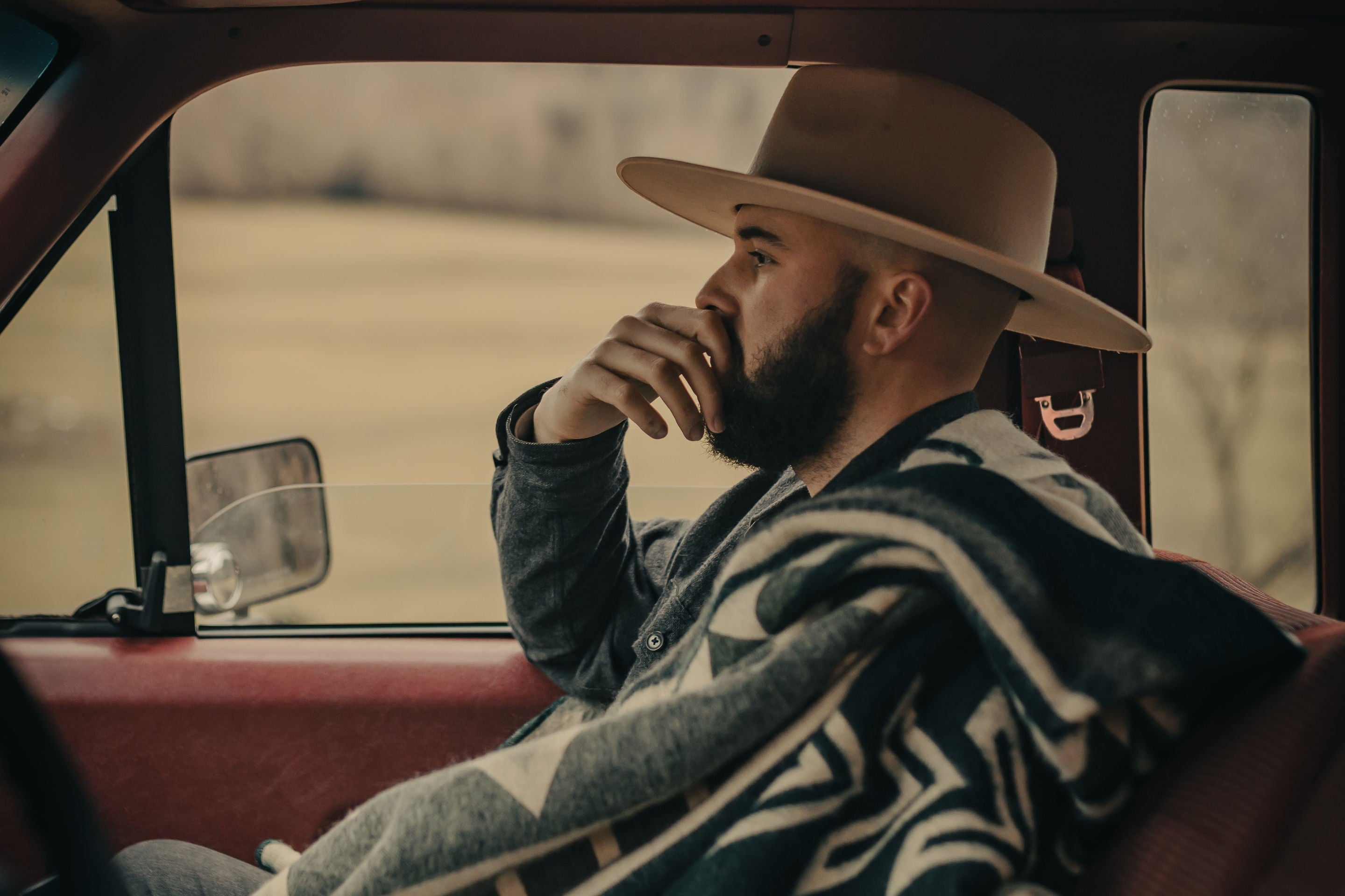 Man sitting in a car with a blanket and hat, looking out the window.