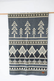 Grey Neutral woven Blanket Hanging on wood display. Trees and Mountain design. 