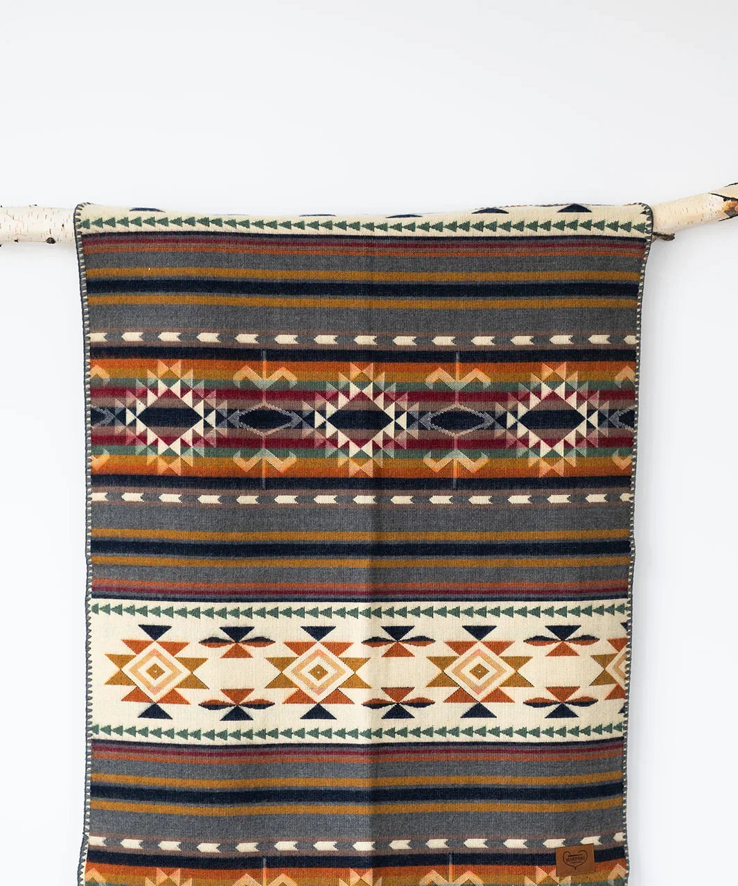 Aztec-inspired patterned blanket with geometric designs in warm earth tones hanging on a branch