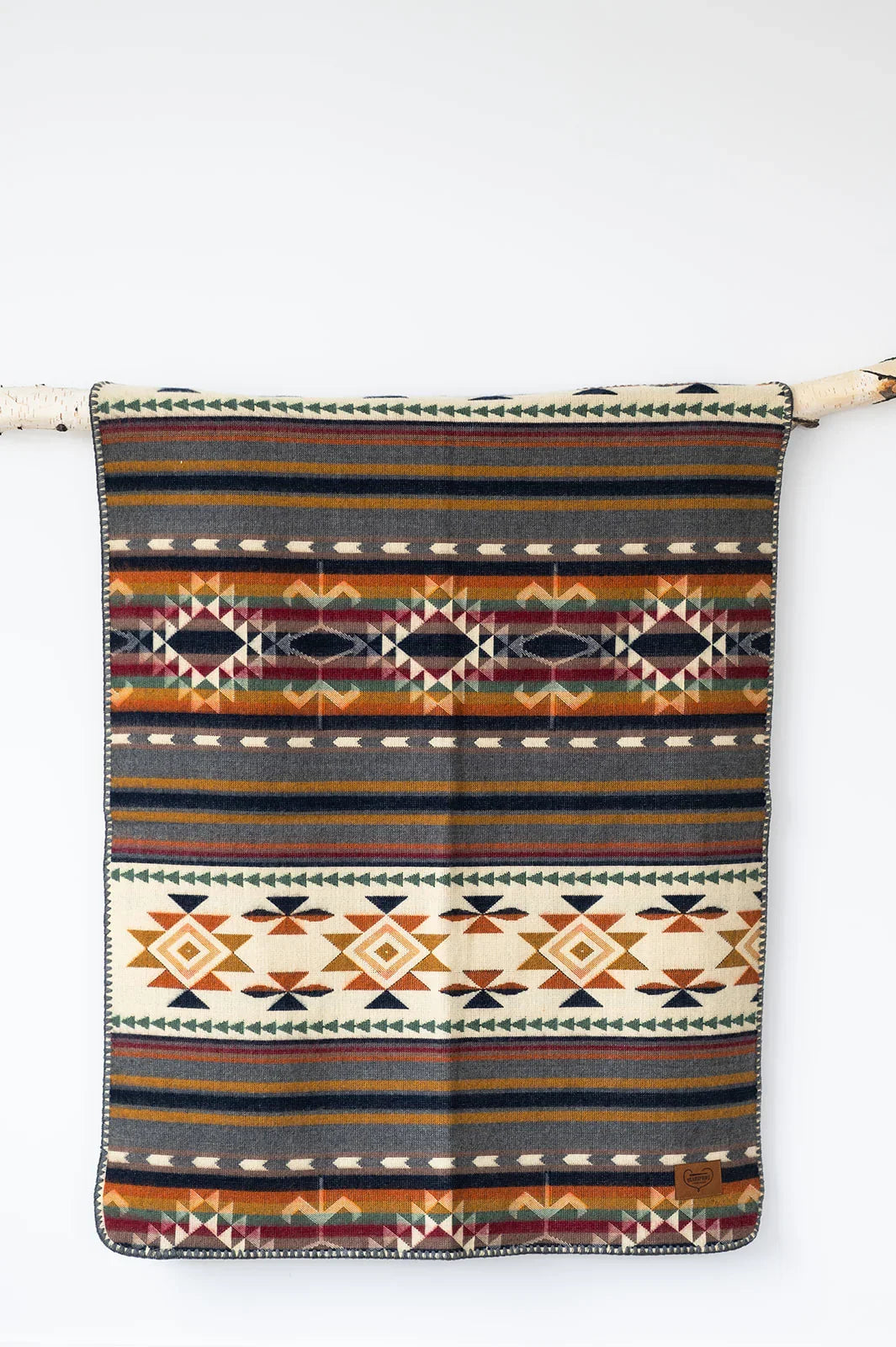 Aztec-inspired patterned blanket with geometric designs in warm earth tones hanging on a branch