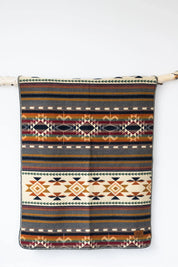Aztec-inspired patterned blanket with geometric designs in warm earth tones hanging on a branch