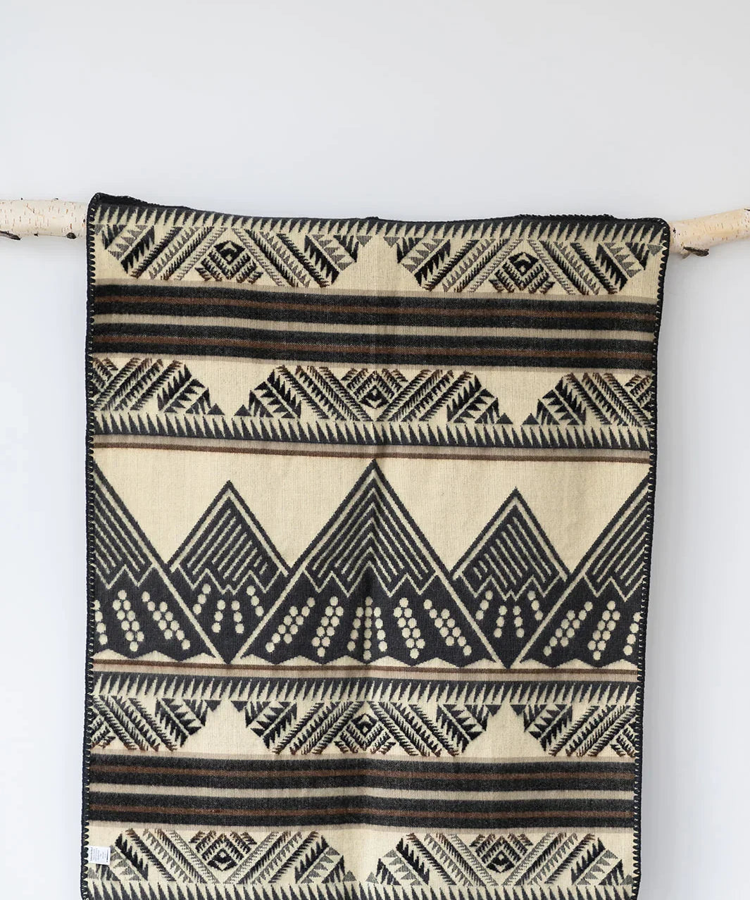 Beige and black geometric patterned woven blanket hanging on a birch wood rod