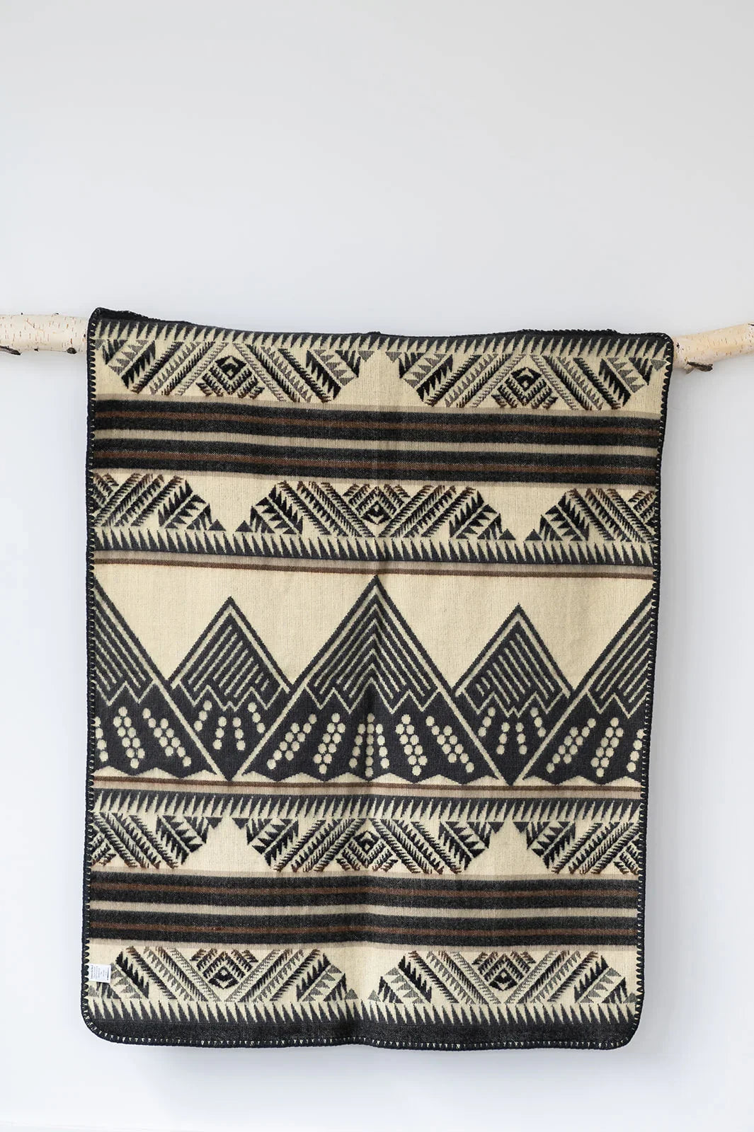 Beige and black geometric patterned woven blanket hanging on a birch wood rod