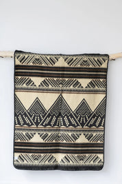 Beige and black geometric patterned woven blanket hanging on a birch wood rod
