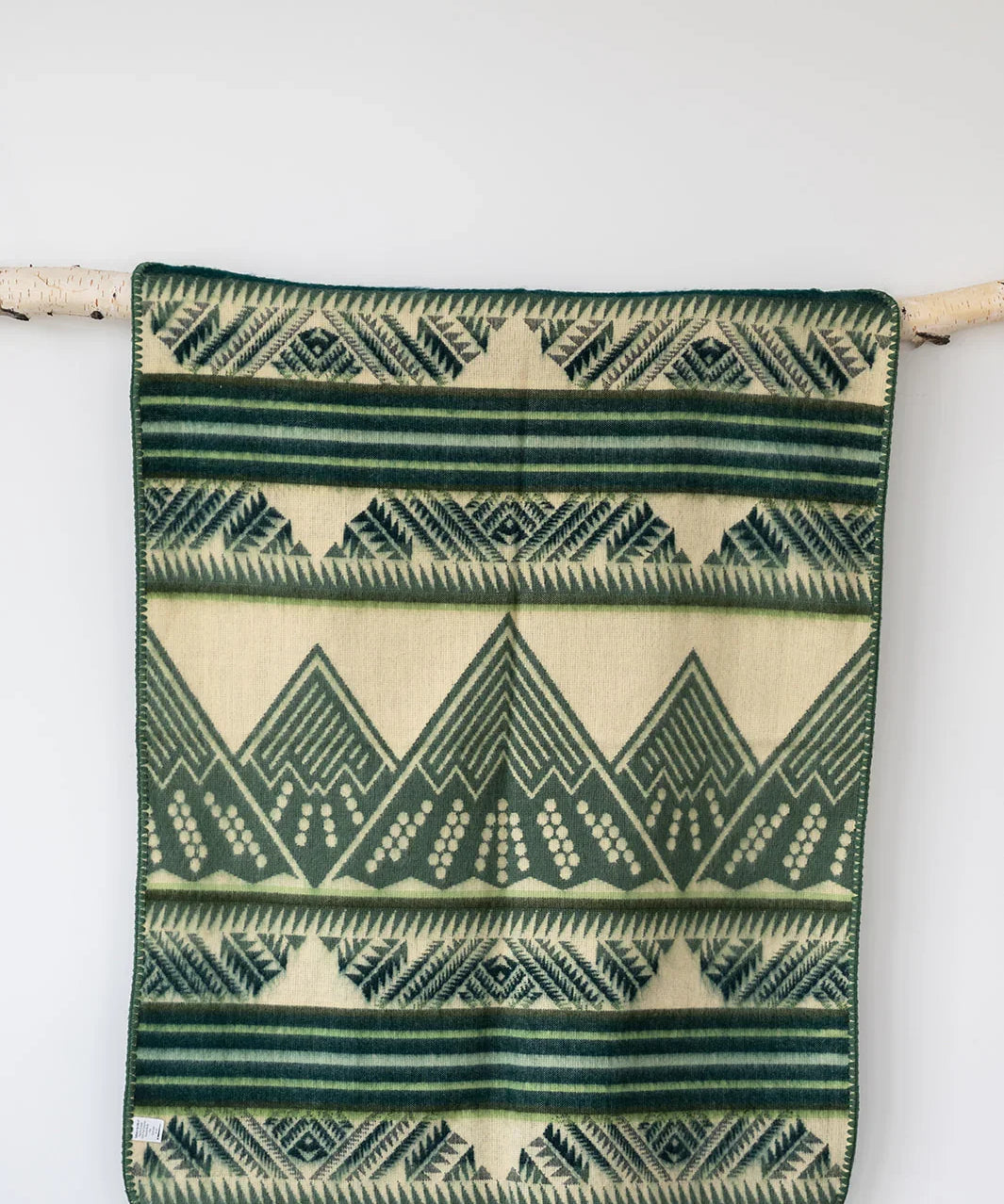 Green and cream geometric patterned throw blanket hanging on a wooden rod