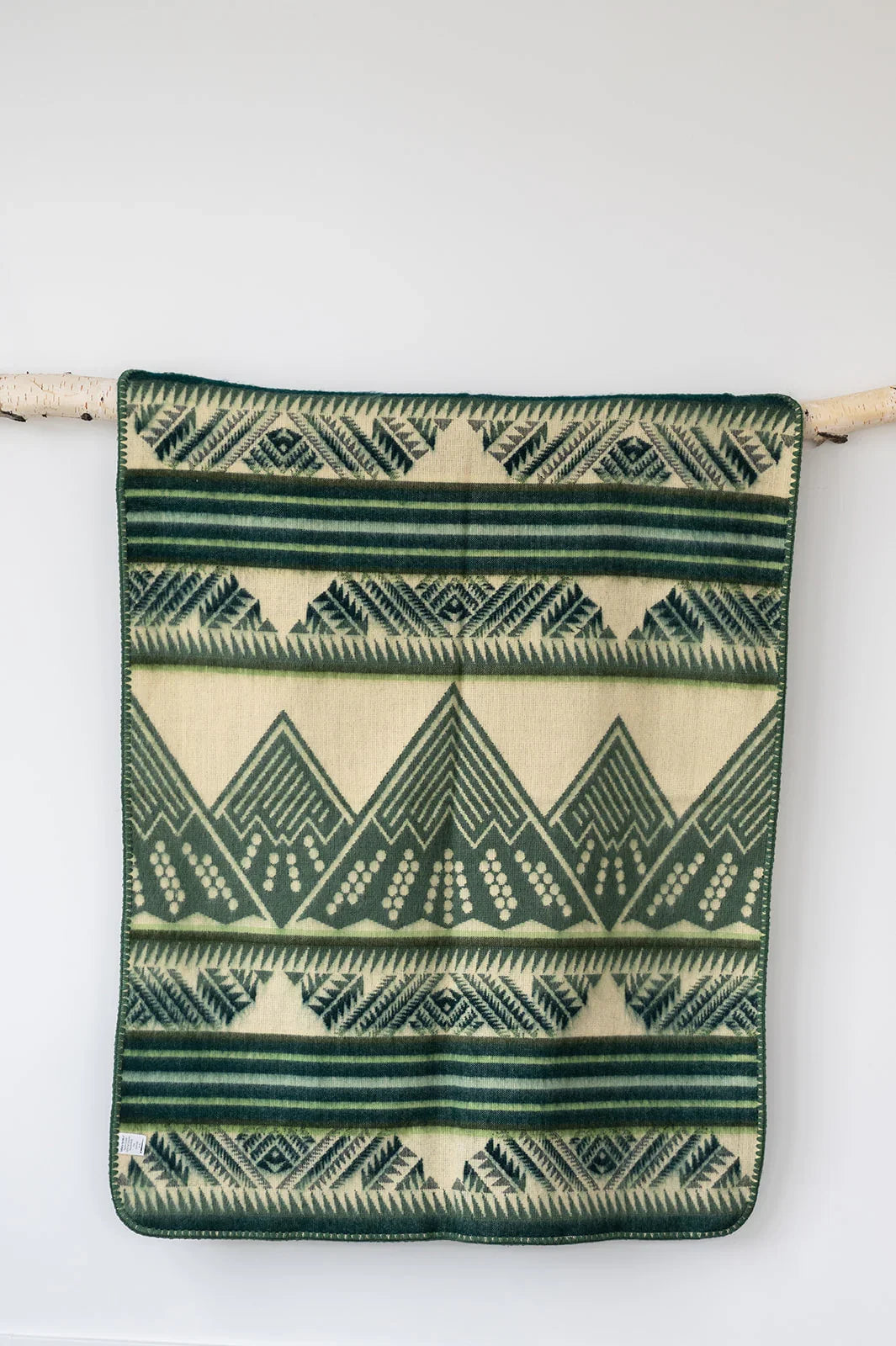 Green and cream geometric patterned throw blanket hanging on a wooden rod