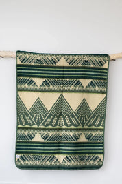 Green and cream geometric patterned throw blanket hanging on a wooden rod