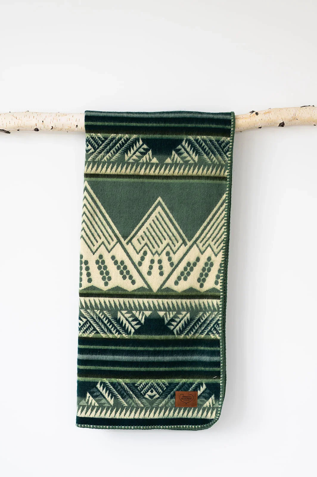 Green and cream patterned throw blanket with geometric mountain design hanging on a birch branch