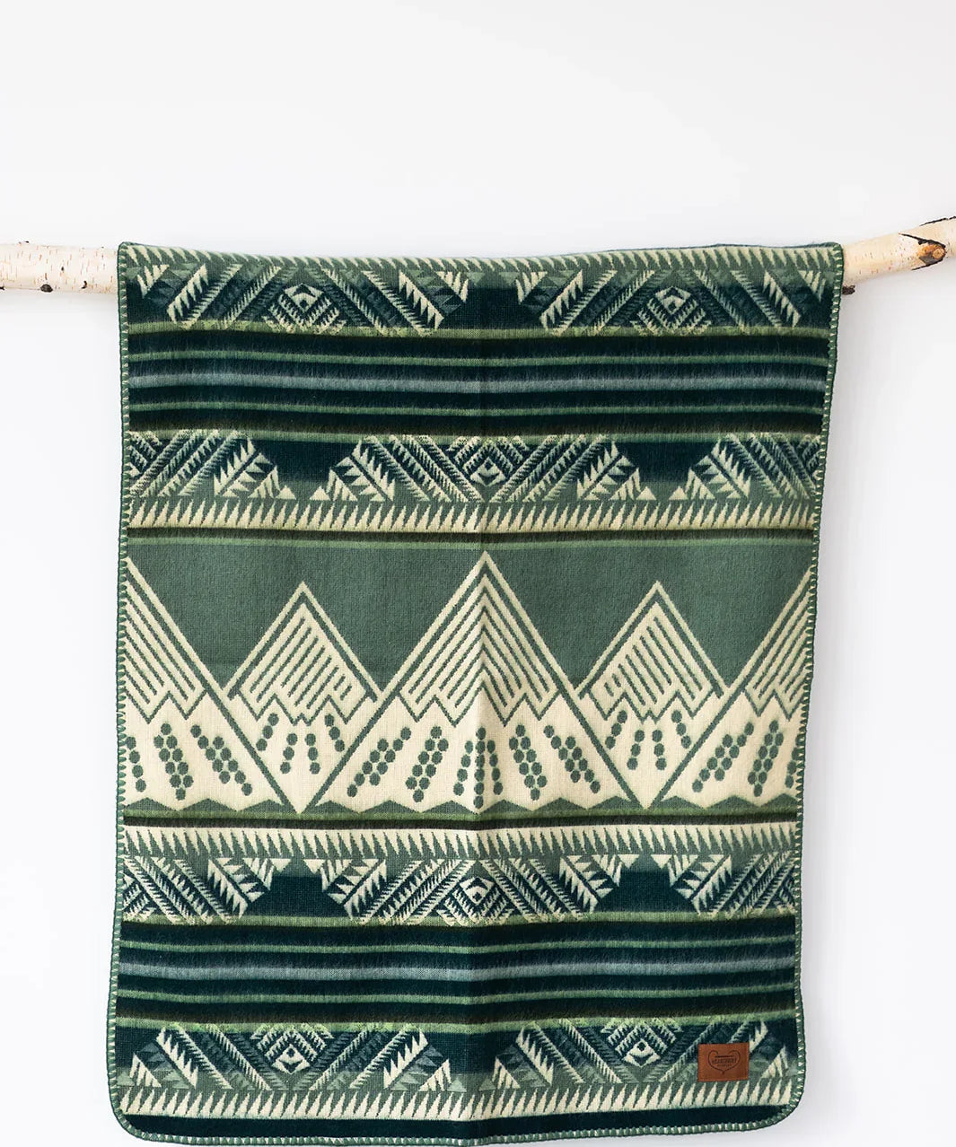 Green and cream geometric patterned throw blanket hanging on a branch against a white wall