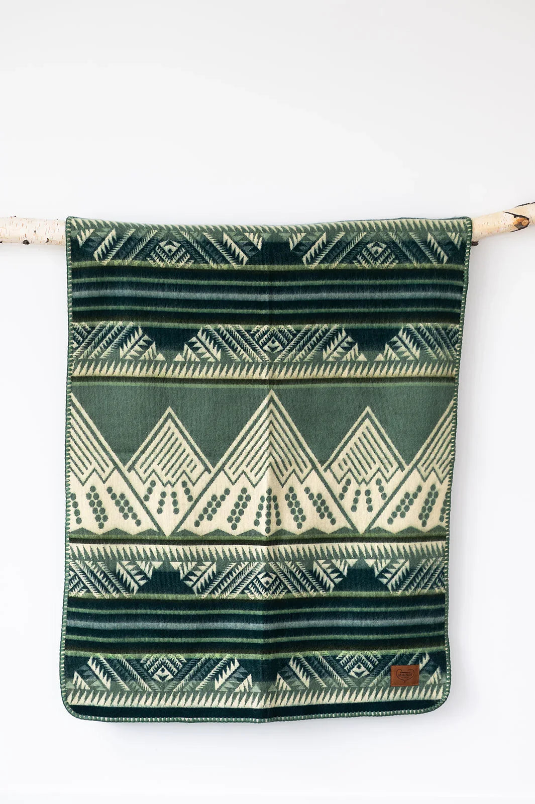 Green and cream geometric patterned throw blanket hanging on a branch against a white wall