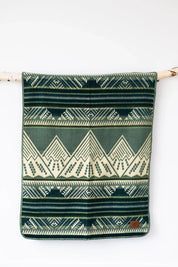 Green and cream geometric patterned throw blanket hanging on a branch against a white wall