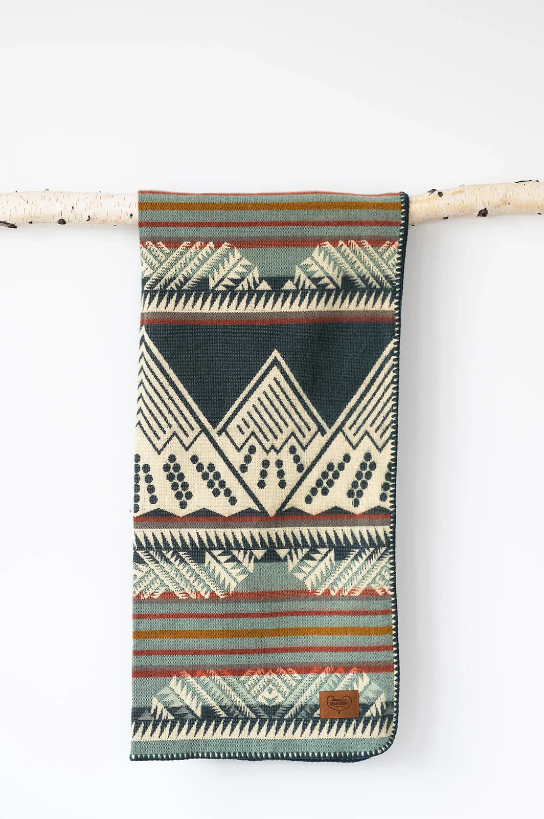 Patterned woven blanket with geometric designs and stripes hanging on a birch branch.