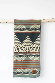 Patterned woven blanket with geometric designs and stripes hanging on a birch branch.