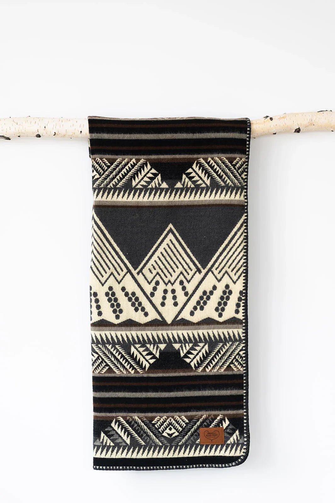 Black and cream geometric patterned blanket with leather patch, hanging on a wooden rod