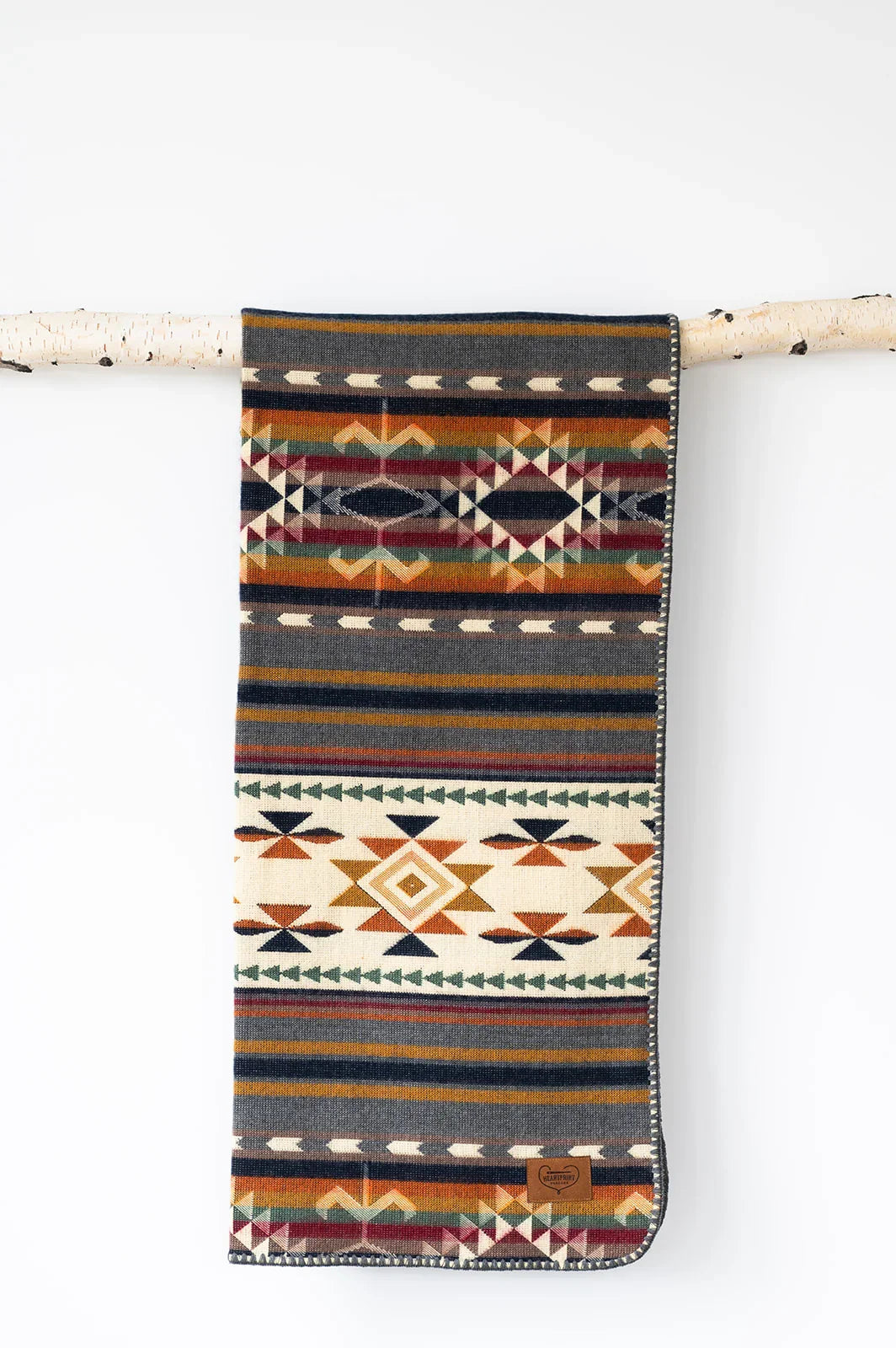 Woven blanket with geometric, Southwestern-inspired patterns and earthy colors hanging on a birch branch