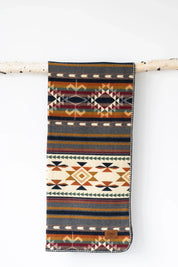 Woven blanket with geometric, Southwestern-inspired patterns and earthy colors hanging on a birch branch