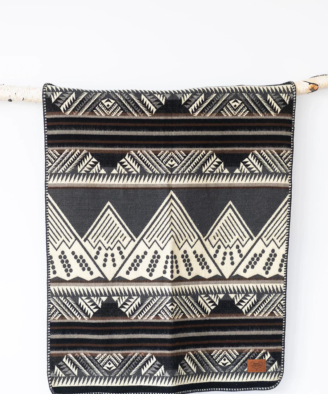 Black and cream geometric patterned blanket with mountain design hanging on wooden rod