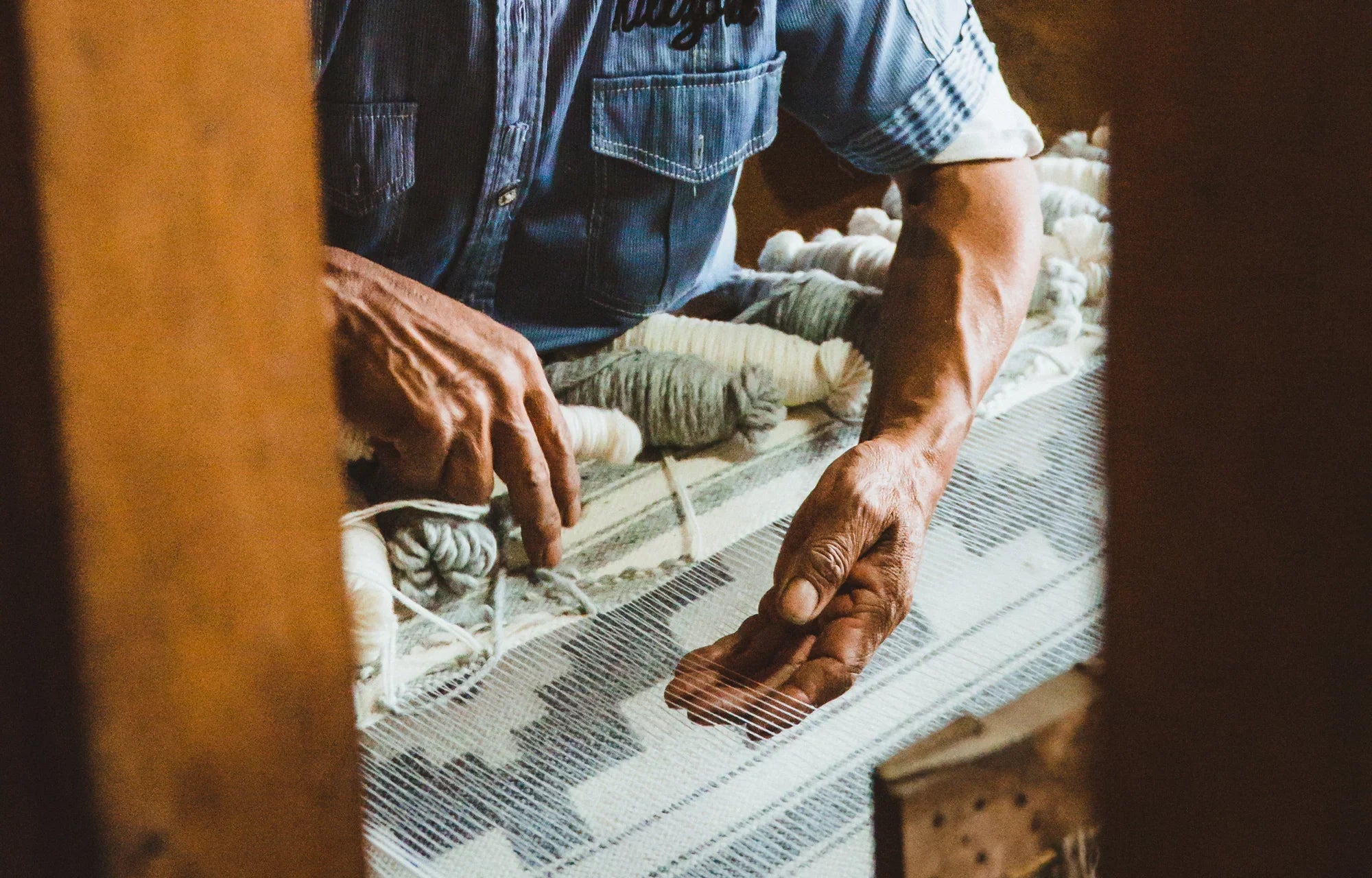 Artisan weaving a patterned blanket by hand on a loom with yarn bundles