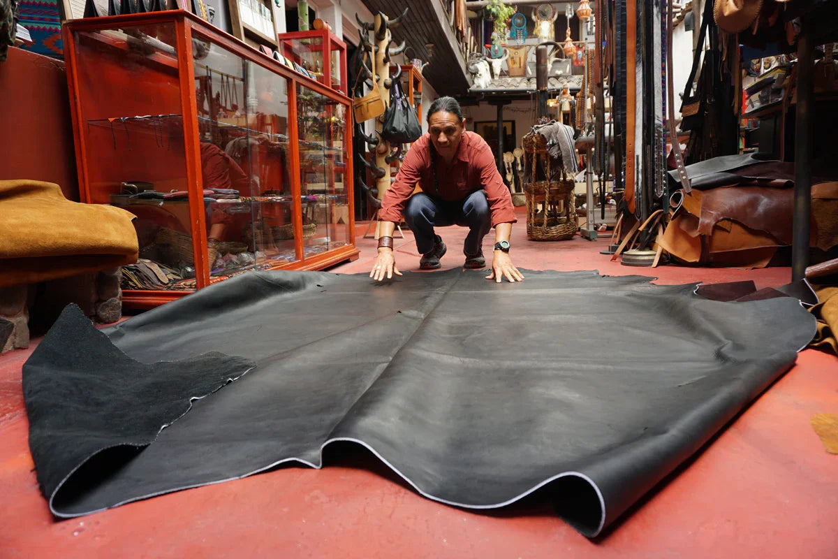 Artisan in workshop arranging large black leather hide on red floor, surrounded by crafts