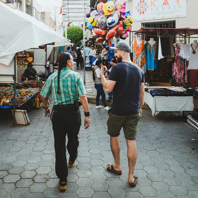 Two men walking through a vibrant outdoor artisan market with colorful products and balloons