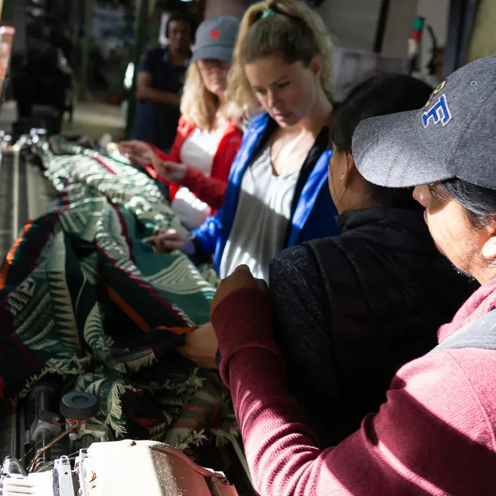 Artisans and workers examining a colorful woven blanket in a workshop setting.