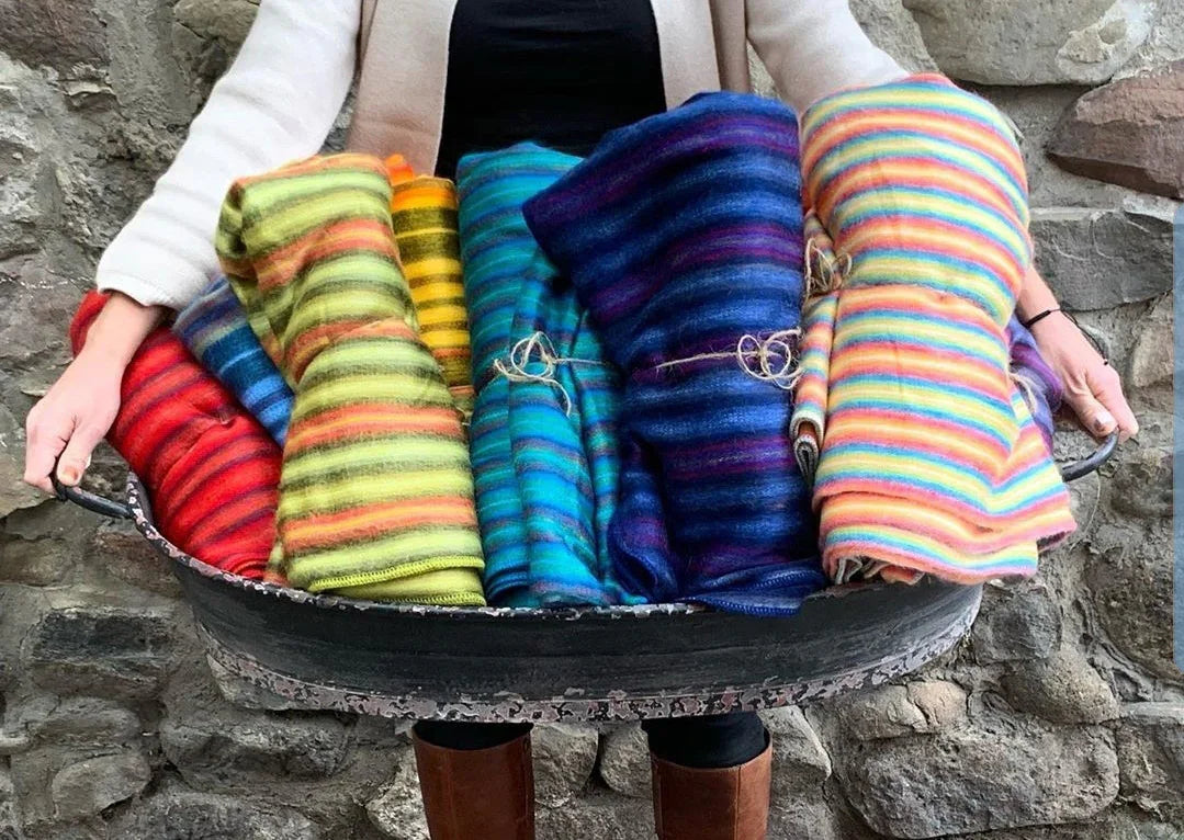 Person holding a basket of colorful striped blankets against a stone wall