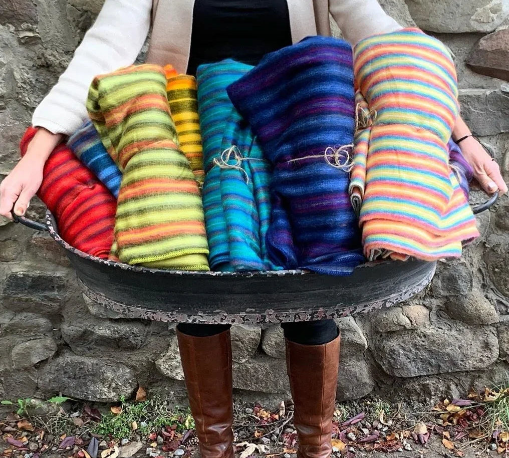 Person holding a basket of colorful striped blankets against a stone wall