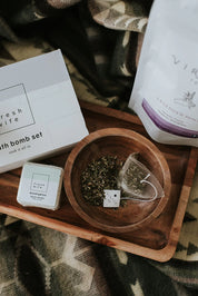 Cozy blanket with bath bomb set, herbal tea bag, and loose leaf tea on wooden tray