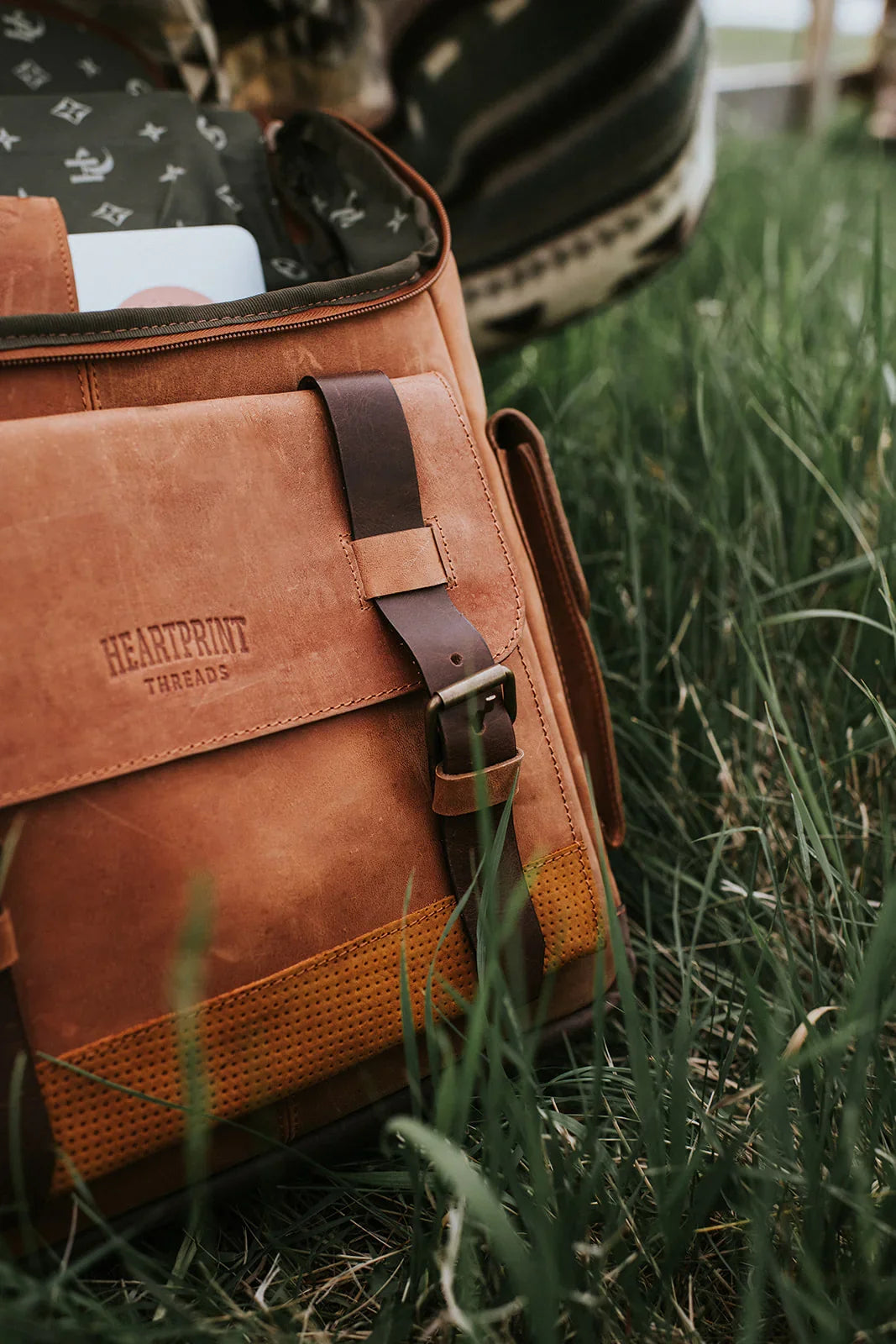 Brown leather messenger bag with buckle detail on green grass outdoors
