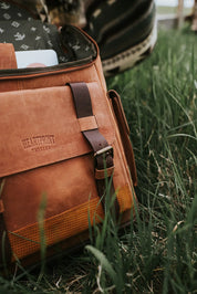 Brown leather messenger bag with buckle detail on green grass outdoors