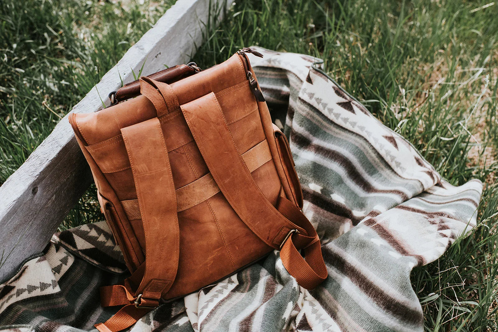 Leather backpack resting on a tribal-patterned blanket in grass outdoors