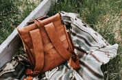 Leather backpack resting on a tribal-patterned blanket in grass outdoors