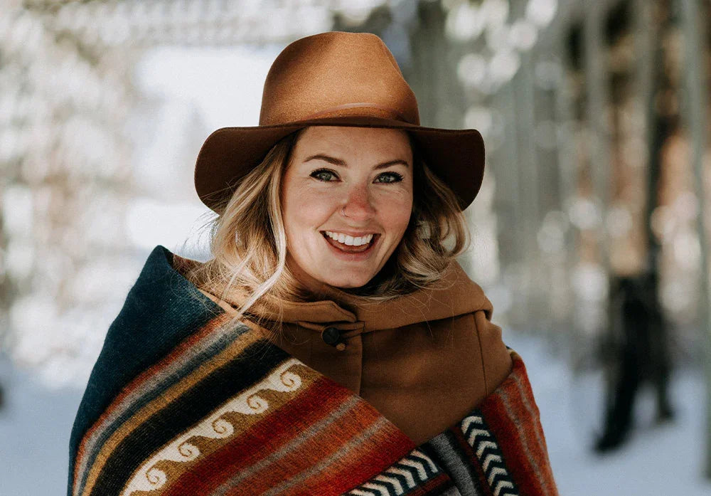 Smiling woman wearing brown hat and colorful patterned blanket outdoors in winter setting