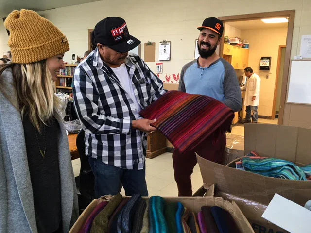Group of people holding colorful handmade blankets in a community donation setting