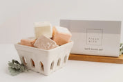 Assorted square bath bombs in a white ceramic basket, with bath bomb set box in background