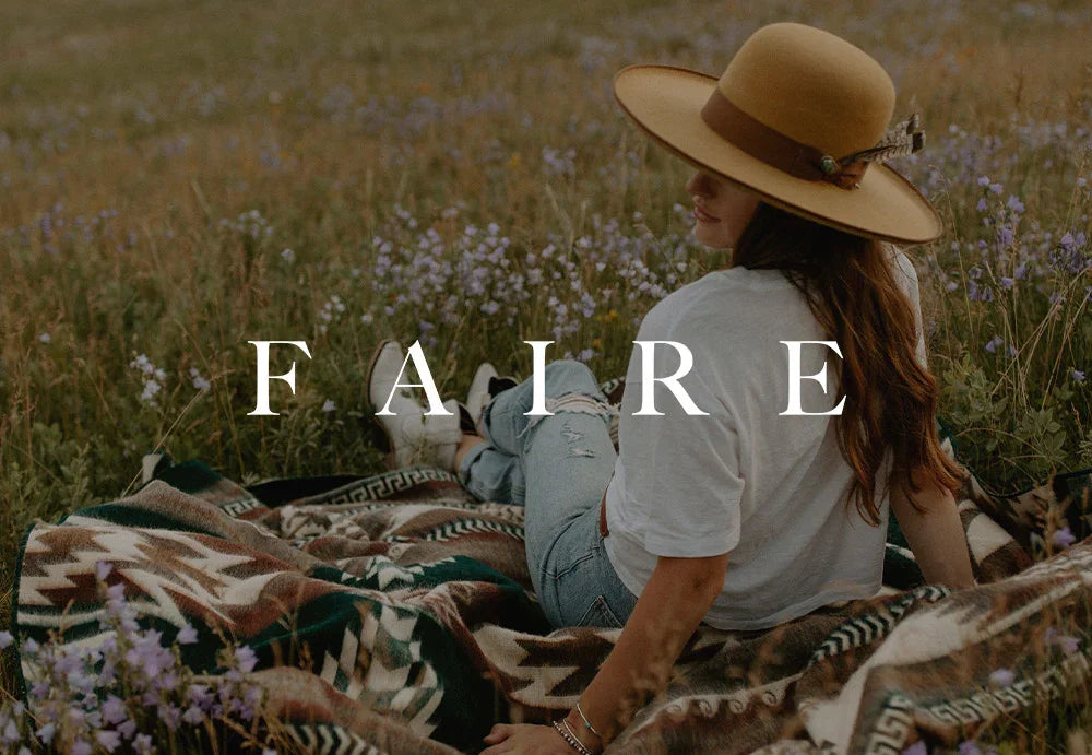Woman in hat sitting on patterned blanket in wildflower field, outdoor comfort vibes