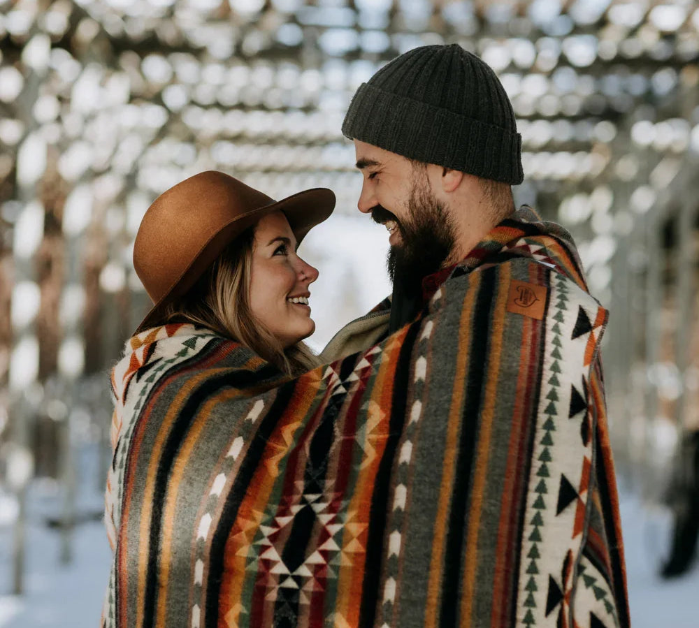 Smiling couple outdoors wrapped in a colorful patterned blanket on a snowy day