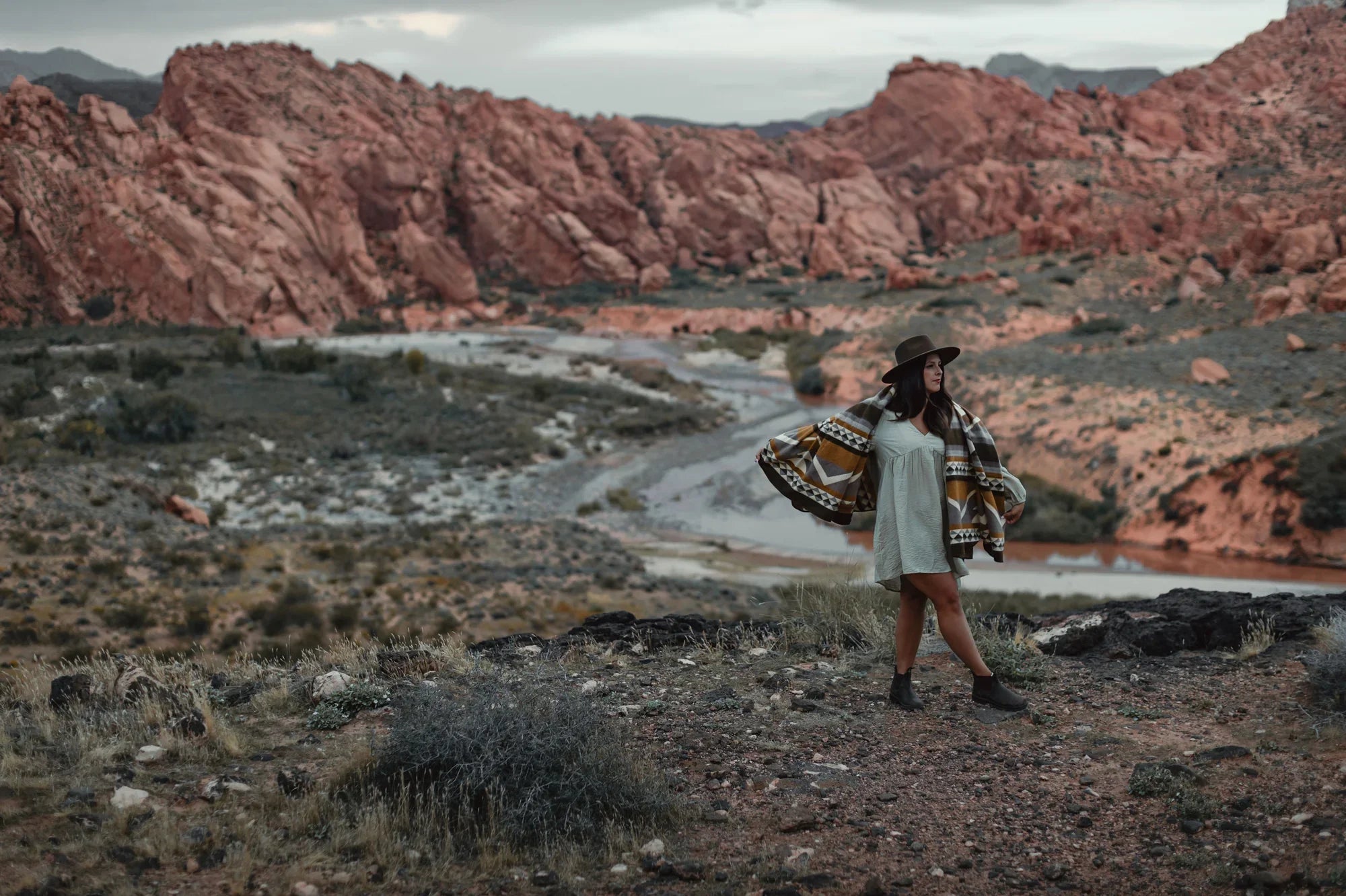 Woman in patterned blanket shawl and hat standing in rocky desert landscape