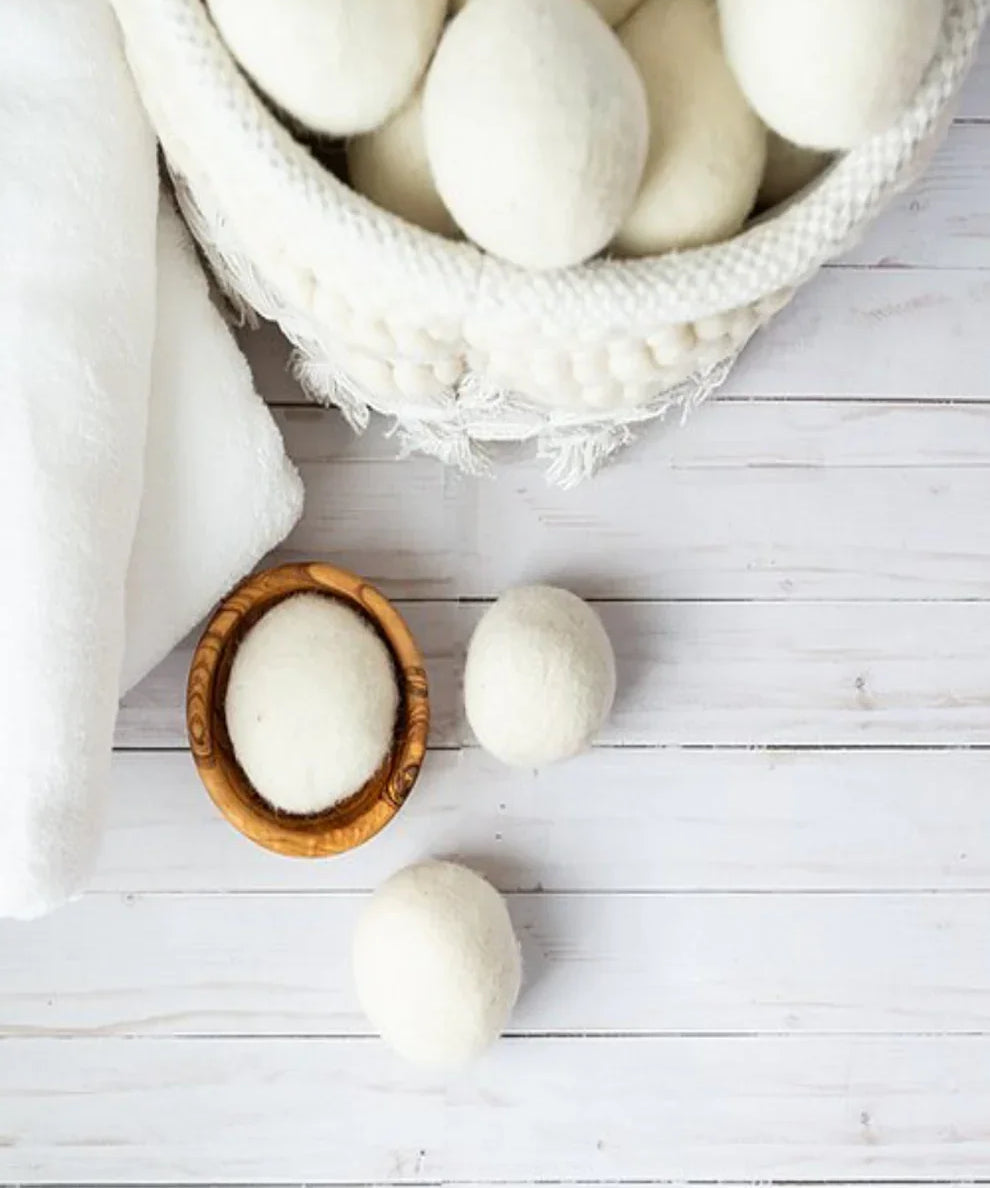 White wool dryer balls in a woven basket with towels on a wooden surface