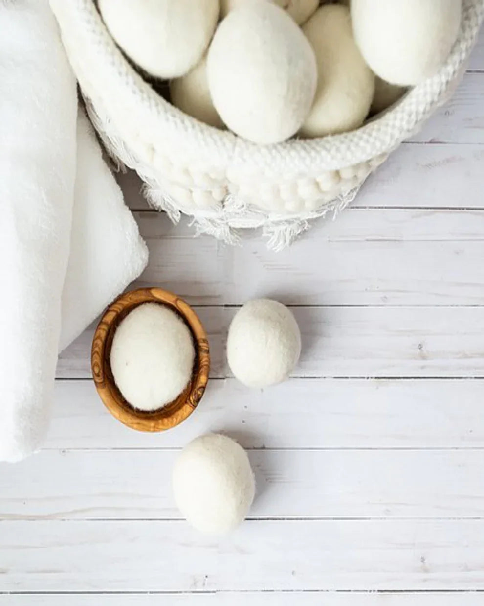 White wool dryer balls in a woven basket with towels on a wooden surface