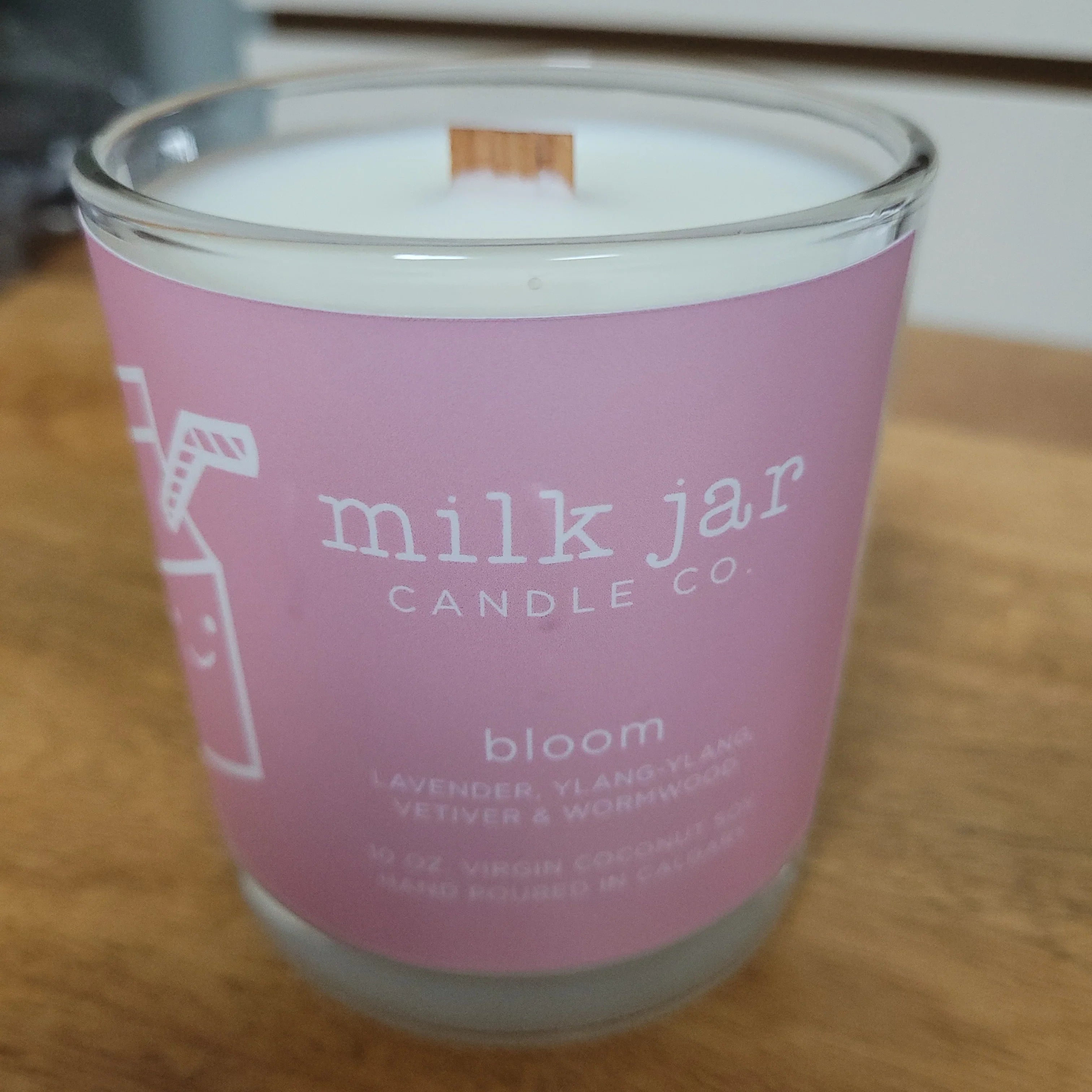 Lavender ylang-ylang scented candle in glass jar with pink label on wooden surface.