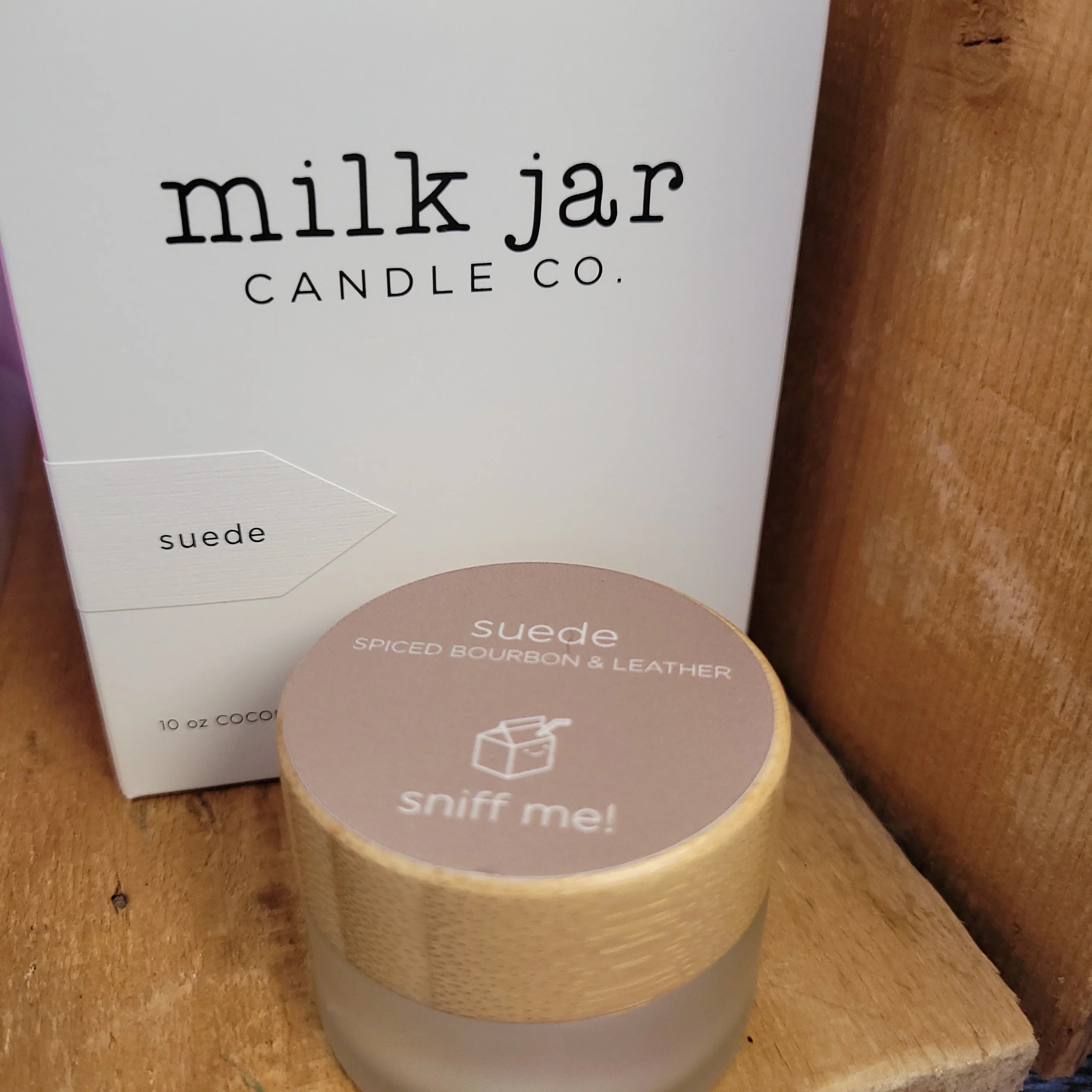 Suede spiced bourbon and leather scented candle in frosted jar with wood lid on wooden shelf