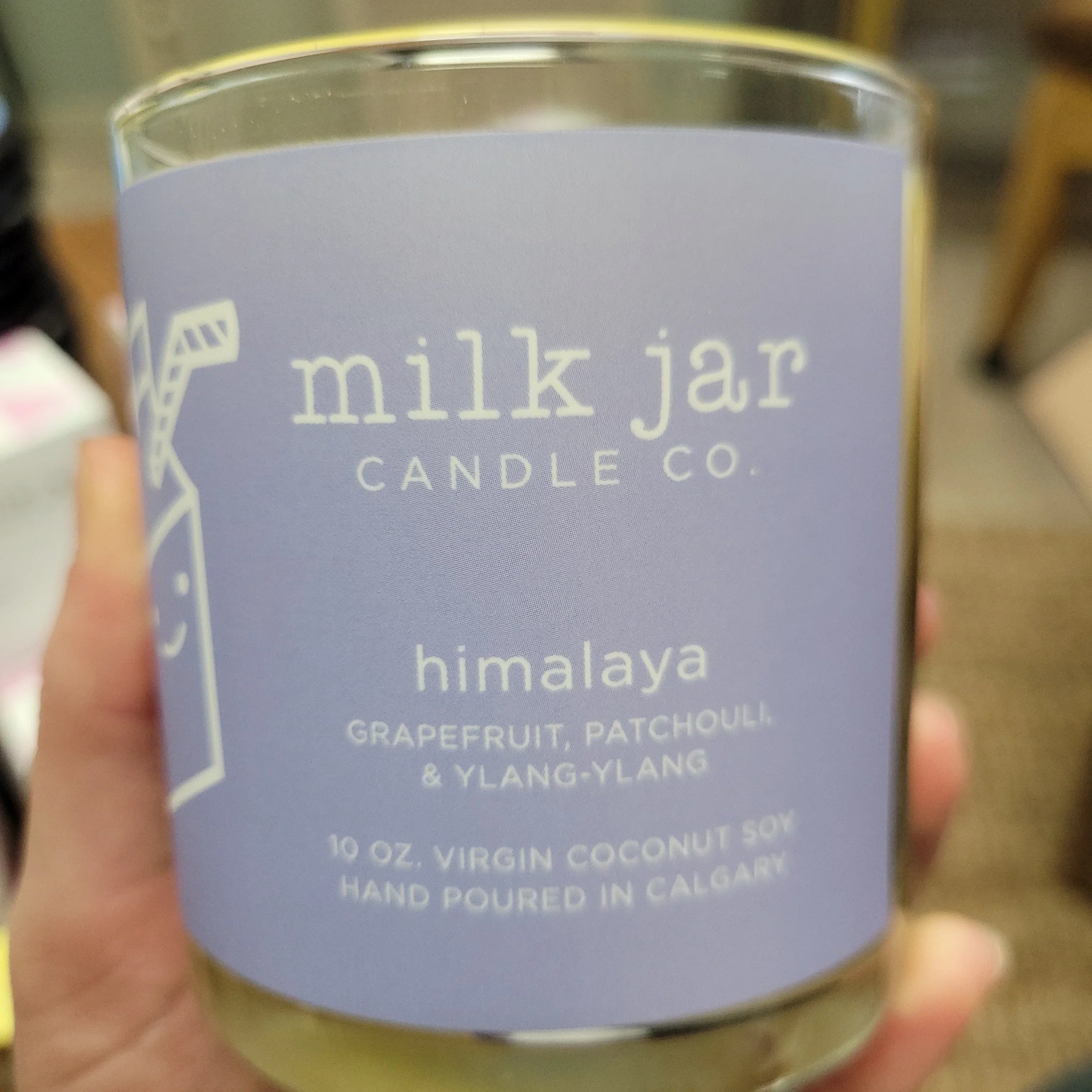 Hand holding a Milk Jar candle, himalaya scent, with purple label and white text.