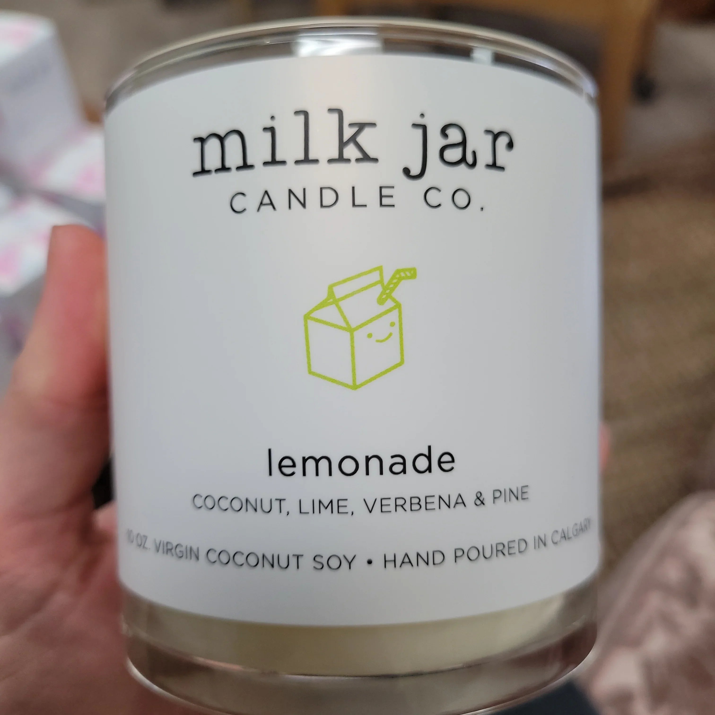 Hand holding a Milk Jar Candle Co. lemonade-scented coconut soy candle with minimalist label.