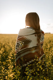 Woman with long braid wearing a patterned blanket in a sunny yellow flower field