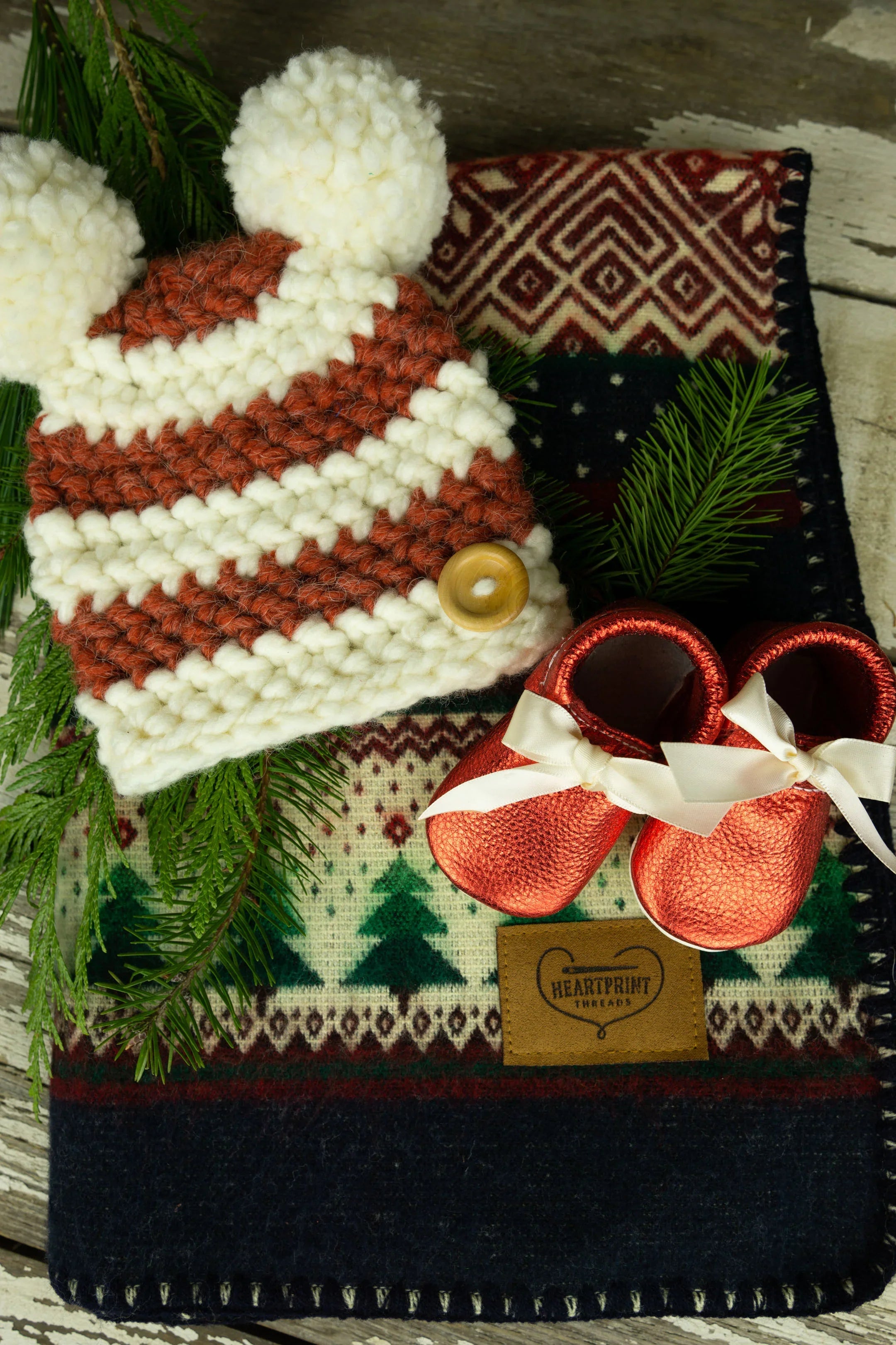 Holiday baby bundle with knit hat, red baby shoes, and festive patterned blanket
