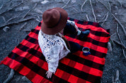 Person sitting outdoors on a red and black buffalo plaid blanket with a coffee mug