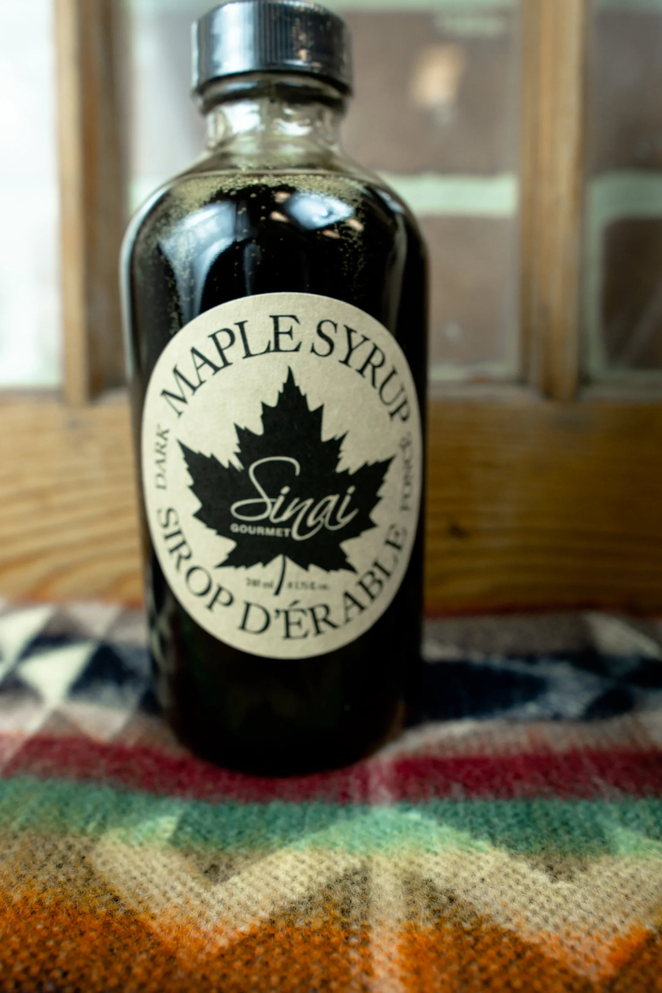 A bottle of dark maple syrup with a maple leaf label on a woven colorful blanket.